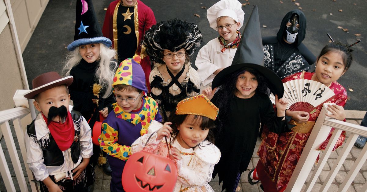 a group of 10 children standing on a front porch dressed in various Halloween costumes and holding candy buckets