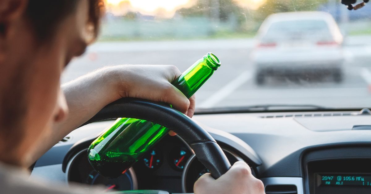 person slumped over a steering wheel holding a beer bottle