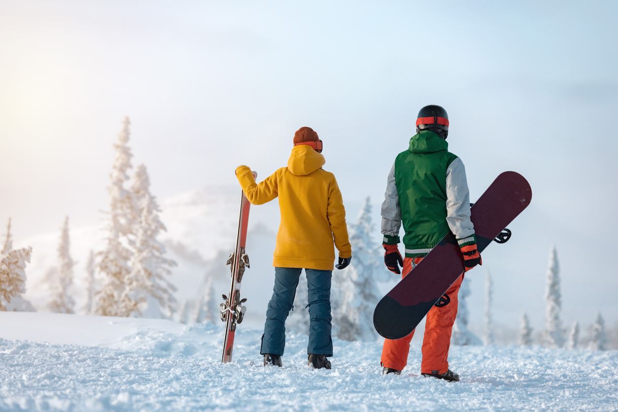 Skier and snowboarder are standing on hill.