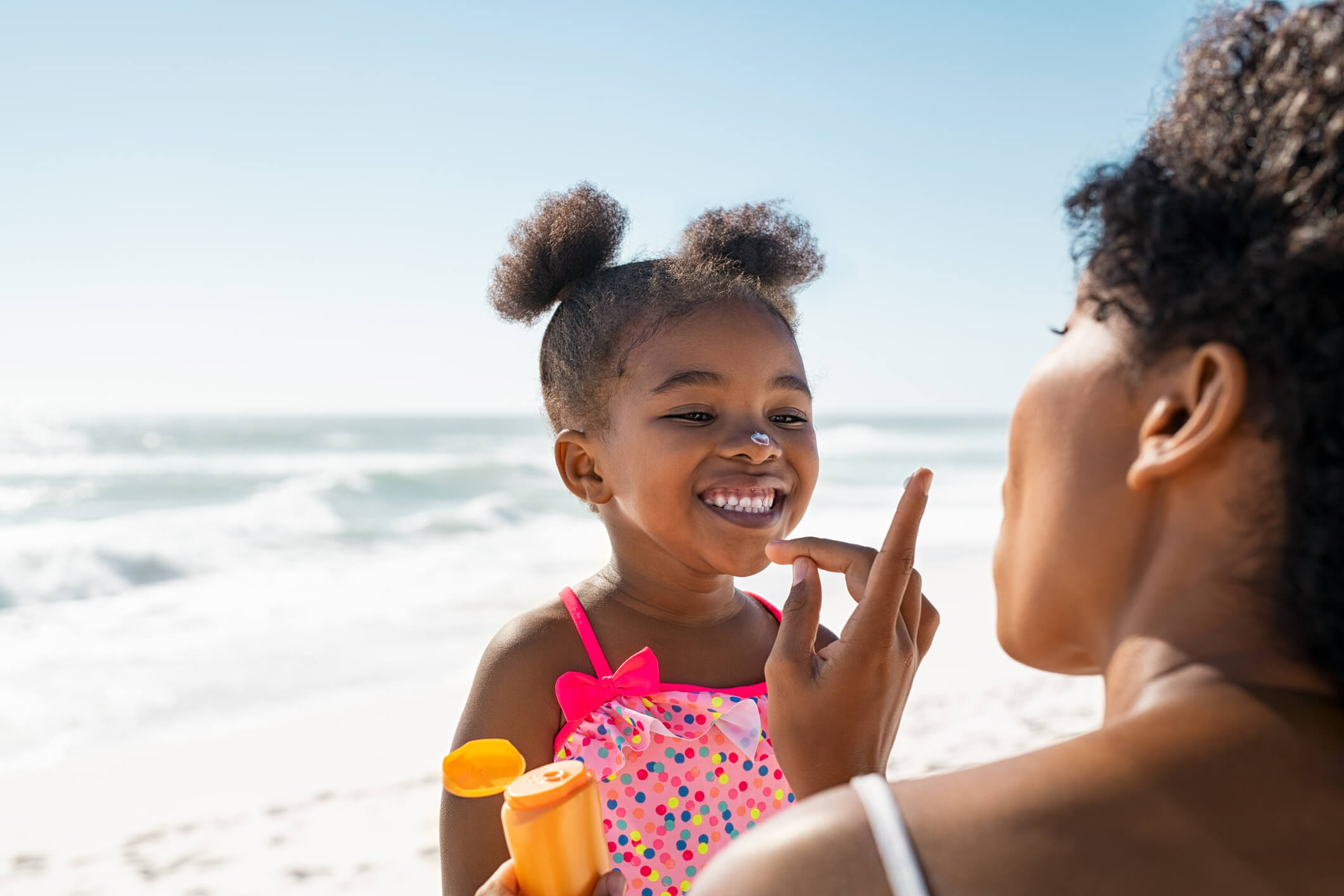 Mother applying sunscreen on daughter at beach