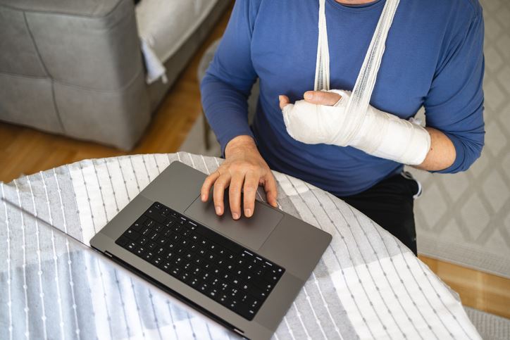 mid-adult Caucasian man, using a laptop while having a hand in the orthopedic cast