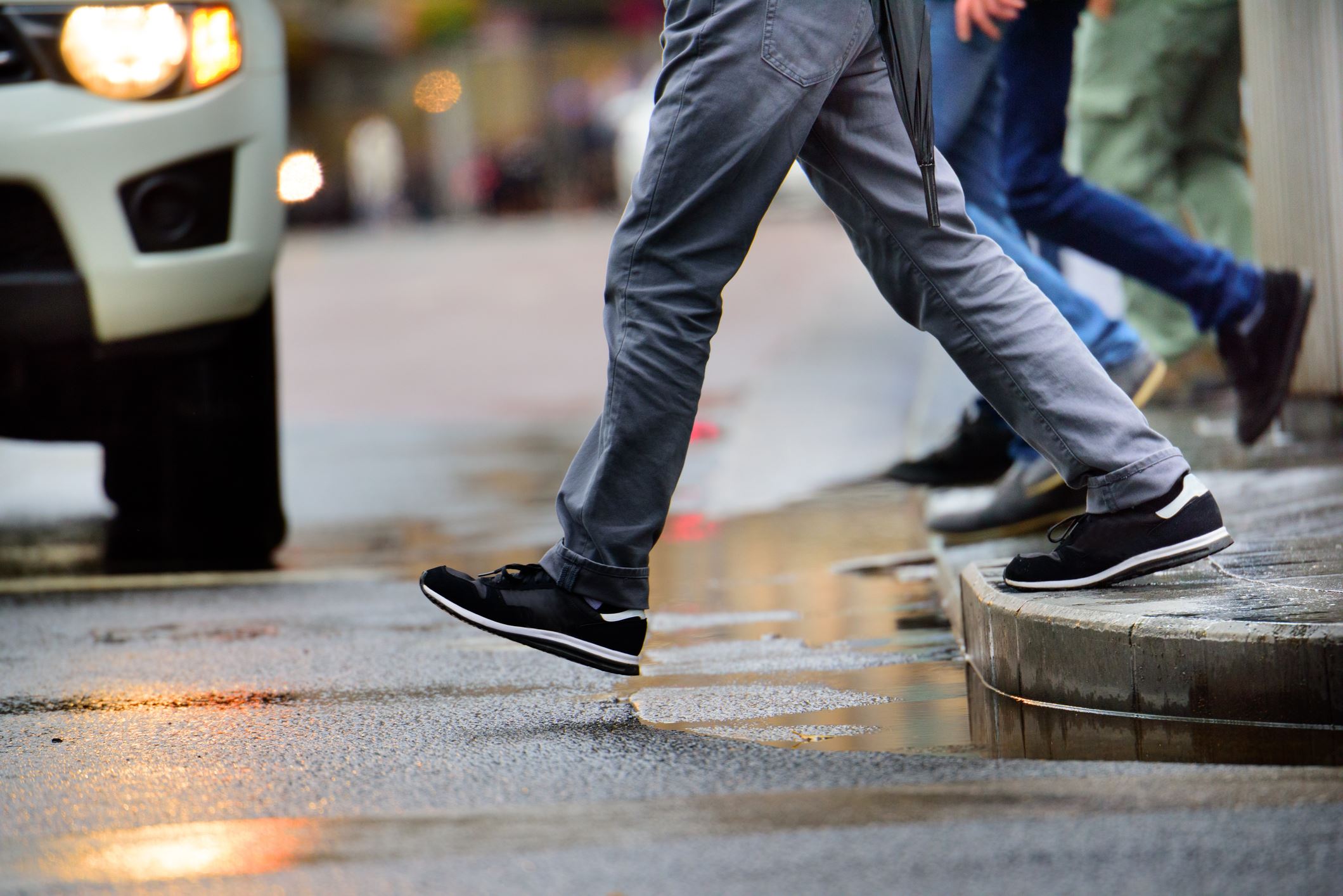 pedestrian walking in front of car in crosswalk rainy pavement