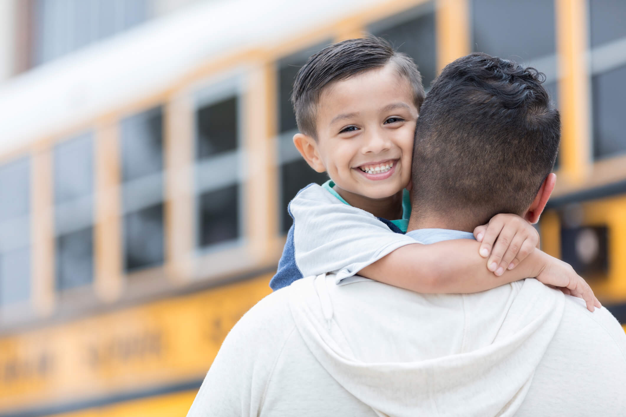 Father hugging son in front of school bus