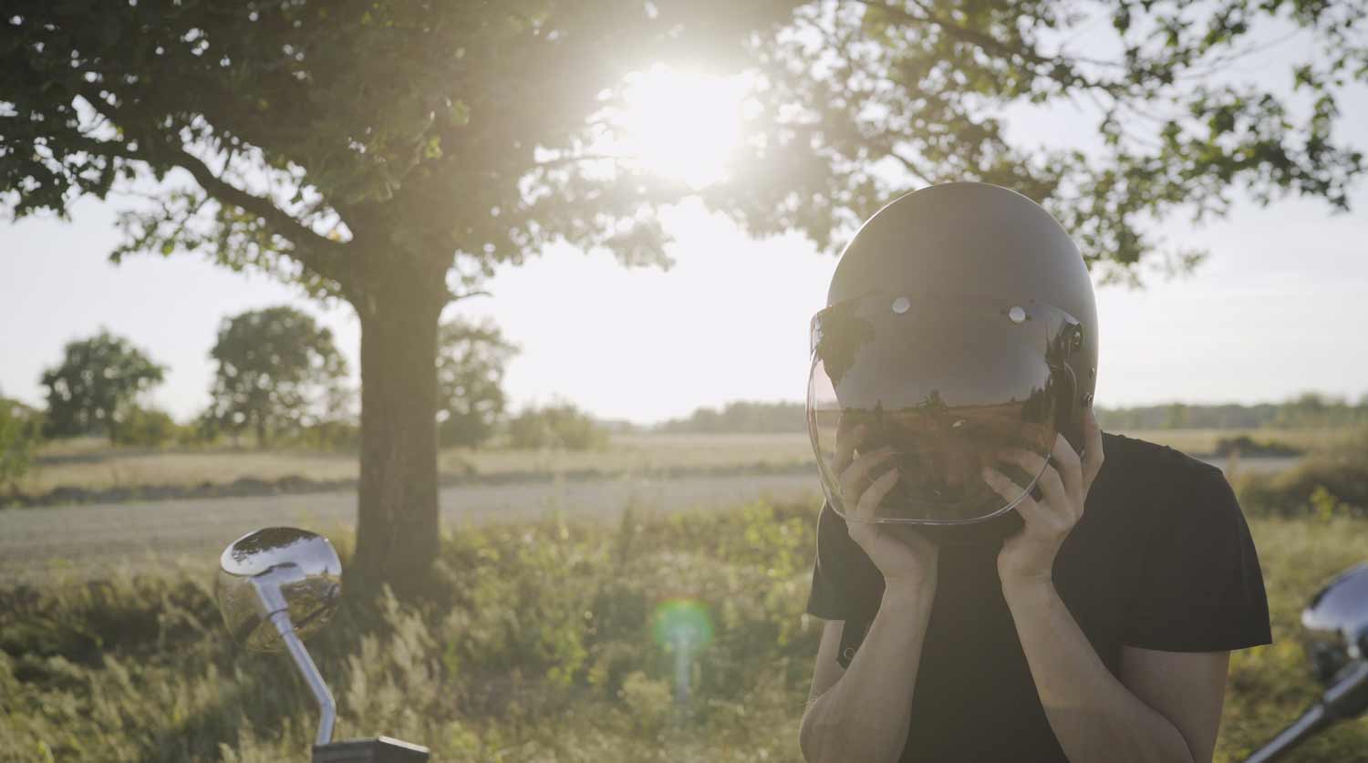 man standing beside his motorcycle taking off his helmet